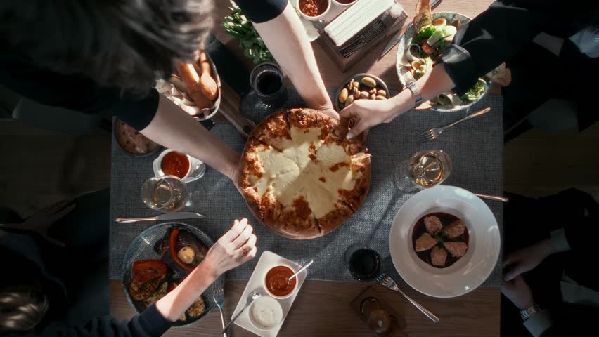 Festive table with many delicious dishes with a large cheese pizza in the middle in a cheerful company of close people. Top shot