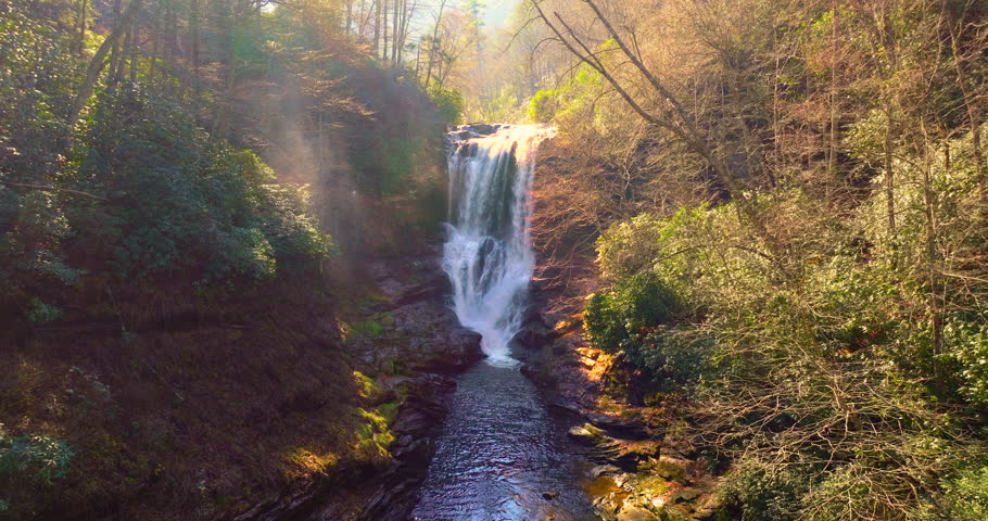 Dry Falls in fall season, nestled in colorful woods of the Nantahala National Forest. Visitors walk behind the waterfall as it flows over mossy rocks