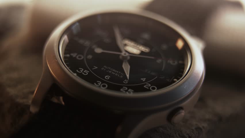 Macro close up of an automatic mechanical field watch with moving arms
