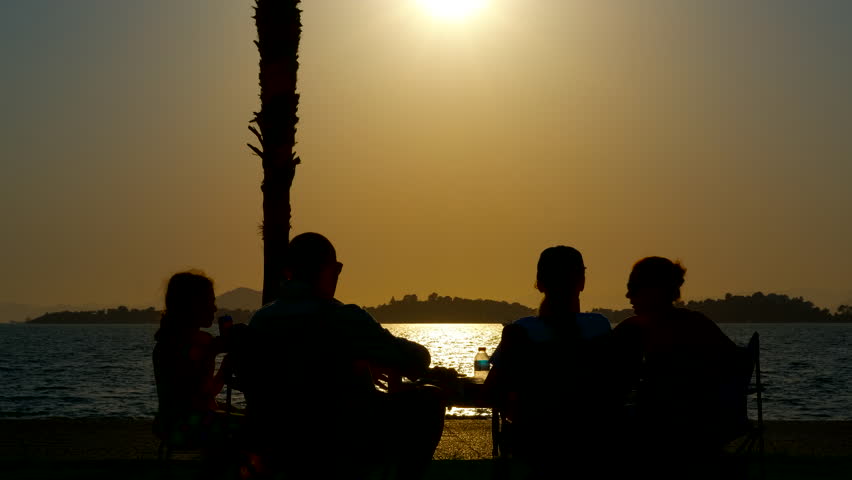 Family enjoying sunset picnic by the sea. Silhouetted family sharing food and drinks during serene seaside picnic, creating lasting memories with warm golden light