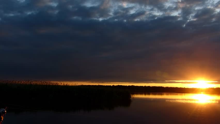 Dark dramatic sunset over a calm lake. A peaceful natural landscape with reeds and a beautiful sky. Serene nature scene at dusk.