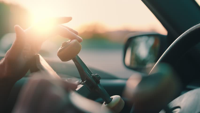 Driver holding skateboard spinning wheel while sitting in car during golden hour sunset with busy highway in background