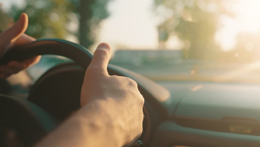 Driver hands nervously tapping fingers on steering wheel during traffic jam at golden hour sunset on busy highway