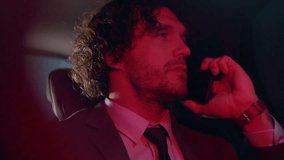 Young business executive in formal suit sitting in back seat of car and speaking on cell phone during night trip, red street lights illuminating his face - Powered by Shutterstock - Get 15% off with code: PIKWIZARD15