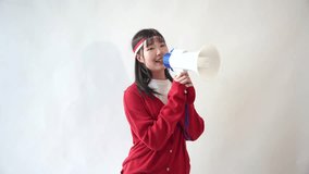 Excited young Asian woman wearing a white t-shirt and red sweater shouts into a megaphone announcing a discount, isolated on a white background. Indonesian Independence Day concept. - Powered by Shutterstock - Get 15% off with code: PIKWIZARD15