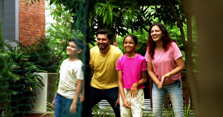 Indian family playing Tennikoit sports outdoor with ring catching game, spending quality time together in park, cheerful Asian parents children enjoying traditional recreational activity on lawn