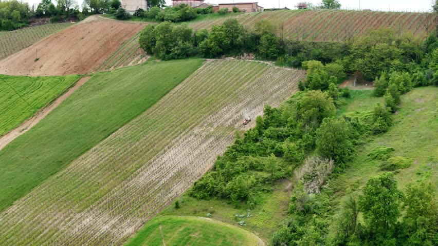 Aerial farmland view showing agricultural tractor spraying pesticides across cultivated landscape with surrounding green fields and vegetation