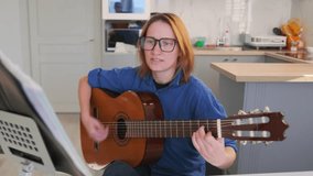 Red-haired woman in glasses plays acoustic guitar and sings during a rehearsal in her kitchen. Casual atmosphere, expressive face, and hand close-ups on strings. Creativity and preparation. - Powered by Shutterstock - Get 15% off with code: PIKWIZARD15