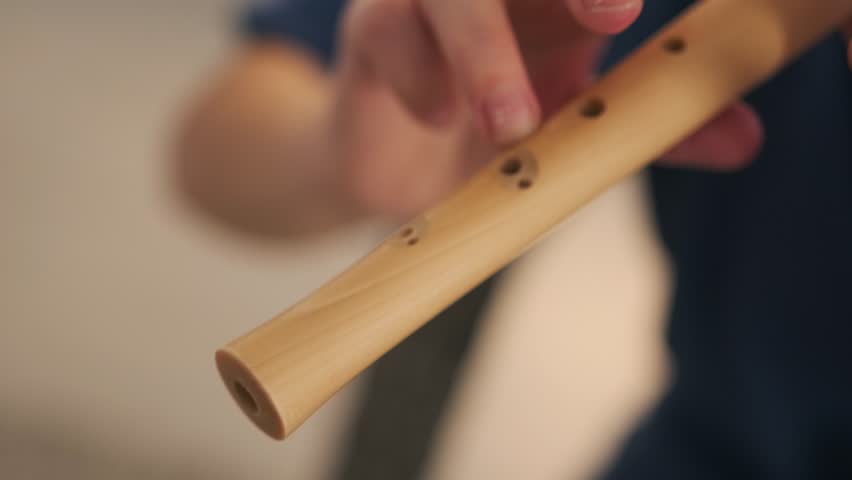 A young woman plays the recorder as part of her creative exploration. Close up. Her focused expression and detailed hand movements reflect musical imagination.