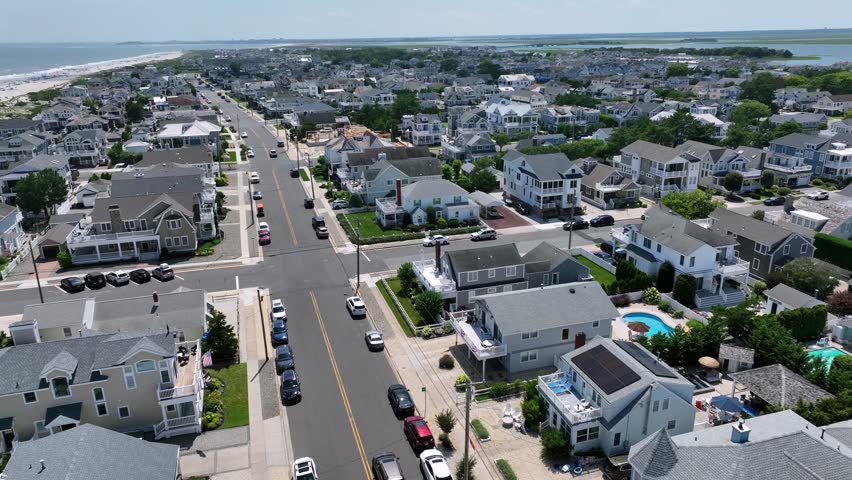 Cityscape of stone harbor with white beach houses and apartments on sunny day. Aerial wide shot. Junction, sandy beach and ocean in New Jersey. Luxury homes in district.