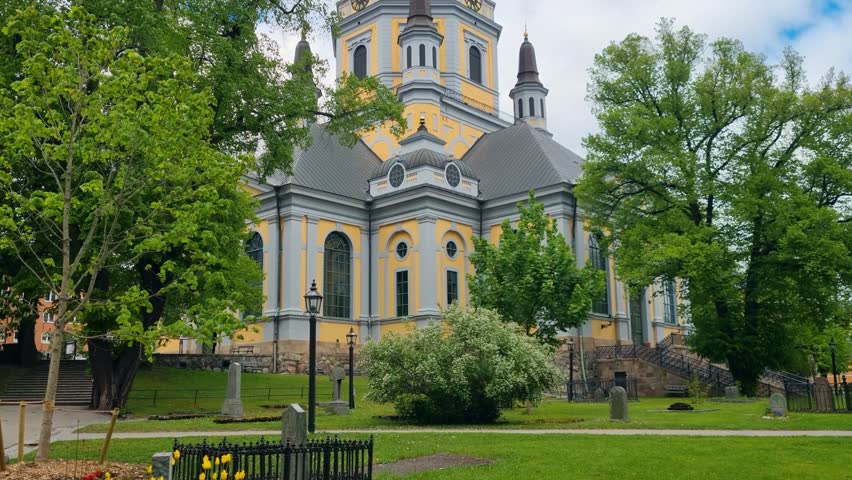 Revealing shot of Katarina Kyrka in the Södermalm district of Stockholm, nestled among lush park vegetation on a partly cloudy spring day