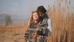 A couple stands in a wheat field with mountains behind. The woman, eyes closed, leans into the man as he kisses her hair and presses his cheek to her temple, sharing affection. - Powered by Shutterstock - Get 15% off with code: PIKWIZARD15