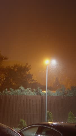 Vertical Screen: Strong winds and heavy rain batter homes and parked cars, creating a dramatic atmosphere under dark clouds with occasional flashes of lightning illuminating the scene.
