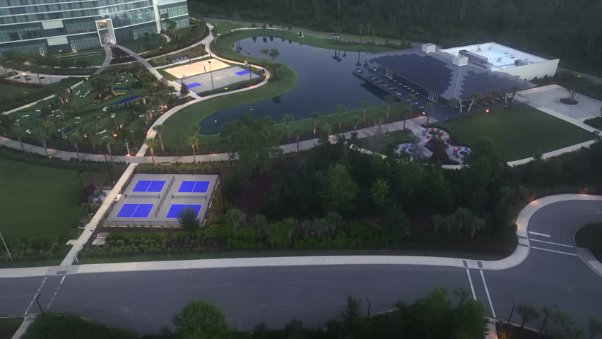 Tennis fields, palm trees, solar panels on roofs and modern company building of KPMG, Orlando. Foggy sunset time in Florida. Aerial tilt up wide shot.