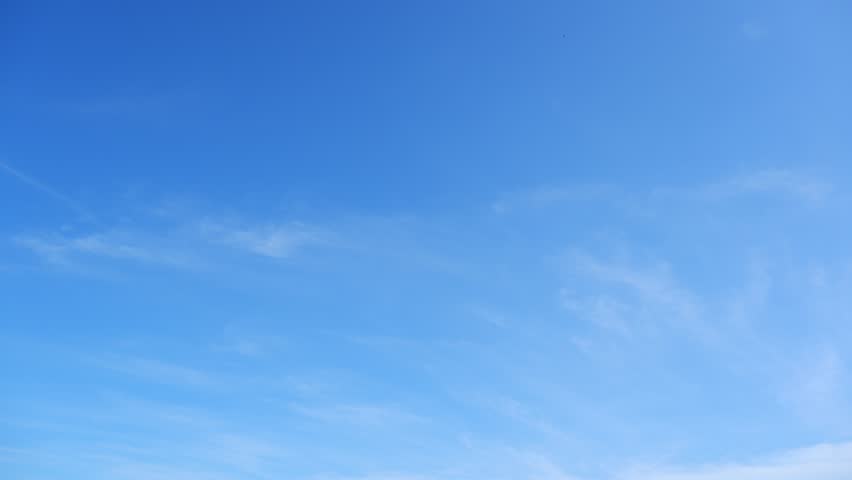 A timelapse captures the sky's gentle dance as wispy clouds flow across a clear blue expanse, showcasing the tranquil, ever-shifting beauty of nature's vast canvas over time. Time-lapse.
