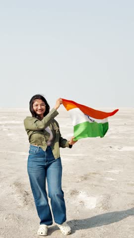 4K Vertical shot of Indian teenager girl holding Indian flag with pride and walking at White Rann Of Kutch, Gujarat, India. Indian woman with Tricolor. Patriotism concept. Independence Day of India. 
