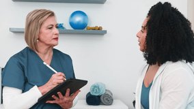 Experienced Senior Physiotherapist Consults Young Black Client with Neck Pain, Taking Digital Notes on Tablet in Her Small Professional Sports Therapy Practice for Injury Assessment and Recovery Plan - Powered by Shutterstock - Get 15% off with code: PIKWIZARD15