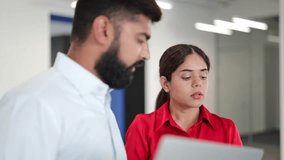 Confident Indian businessman and confident Indian businesswoman, dressed in formal attire, are focused on a laptop and documents in a bright modern office, discussing work with serious expressions. - Powered by Shutterstock - Get 15% off with code: PIKWIZARD15