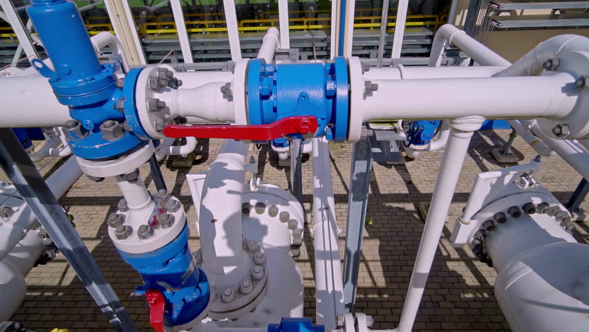 Industrial Pipelines with Blue Valves and a Red-Handled Lever are Arranged within a Paved Processing Facility - Pan Right Shot