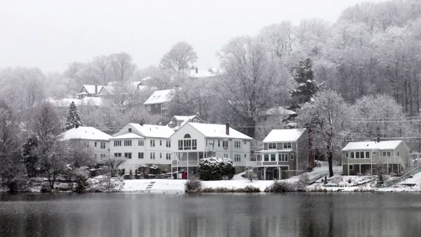 A winter wonderland scene of snow covered houses along a lake in the countryside