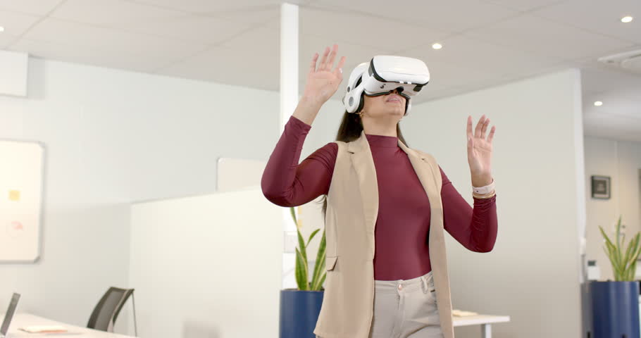 Mid adult woman donning VR headset and navigating menus and exploring simulation in open office. Futuristic, innovation, technology, collaboration, workspace, immersive, digital