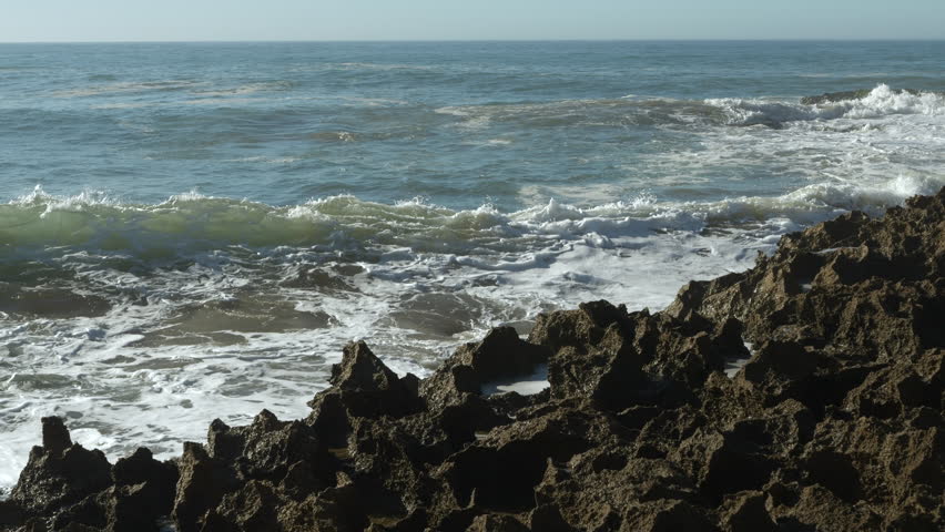 CLOSE UP, SLOW MOTION: Powerful wave crashes against a formation of dark, jagged rocks, sending a massive plume of white spray and foam high into the air. Raw force and energy of the Atlantic Ocean.