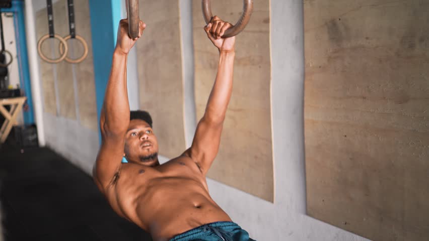 Focused Black man with athletic build preparing for gymnastic ring exercise in modern training facility with concentration