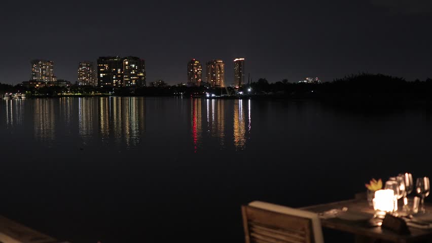 A tranquil scene showcasing a city skyline illuminated at night, with reflections shimmering on the calm water surface.