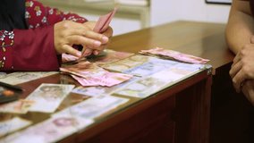Close-up shot of a money changer counting neat stacks of Indonesian rupiah banknotes on a glass counter, illustrating finance, budgeting and currency exchange concepts. - Powered by Shutterstock - Get 15% off with code: PIKWIZARD15