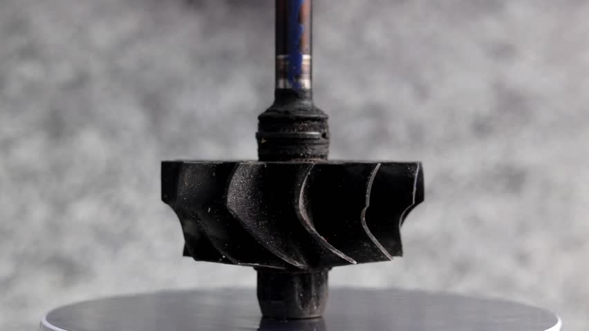 Damaged turbocharger turbine wheel shaft with black blades from carbon residue from combustion.