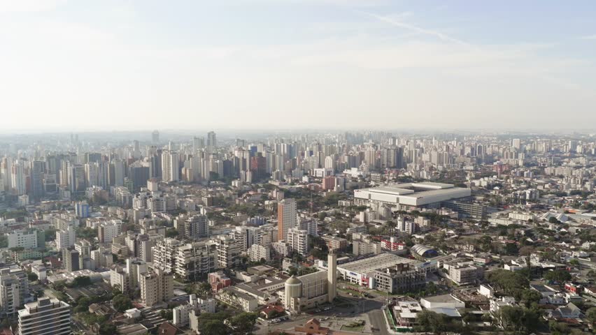 Drone view of Curitiba city skyline with Arena da Baixada stadium visible among the tall buildings.