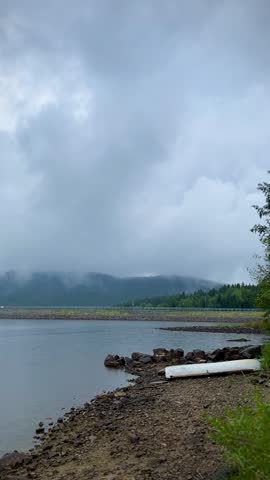Empty canoe lies on rocky lake shore under cloudy sky after rainfall. Overcast weather, moody landscape. Outdoor travel and wilderness theme.