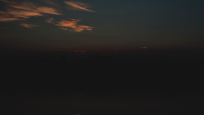 Beautiful time-lapse stock footage of a sunrise. This wide shot shows the sun rising over a reflective mirrored lake, illuminating the sky with orange and yellow light. The clouds move slowly across the sky. This video would be perfect for projects related to nature, time, and the environment. The serene scene is a perfect opening for meditation videos.