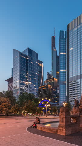 The Fairy-tale Fountain (Marchenbrunnen) before the Central European Bank in Frankfurt transitions from day to night timelapse hyperlapse, casting art-nouveau charm alongside illuminated skyscrapers