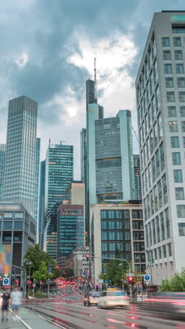 Looking up perspective at glass skyscrapers in Frankfurt's Innenstadt district timelapse. Towering modern architecture reflects rainy clouds across the skyline. Traffic on a crossroad. Germany.