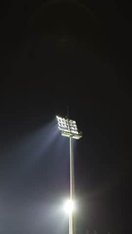 Bright stadium floodlight tower shines into the dark night sky illuminating the surrounding area with powerful beams of light