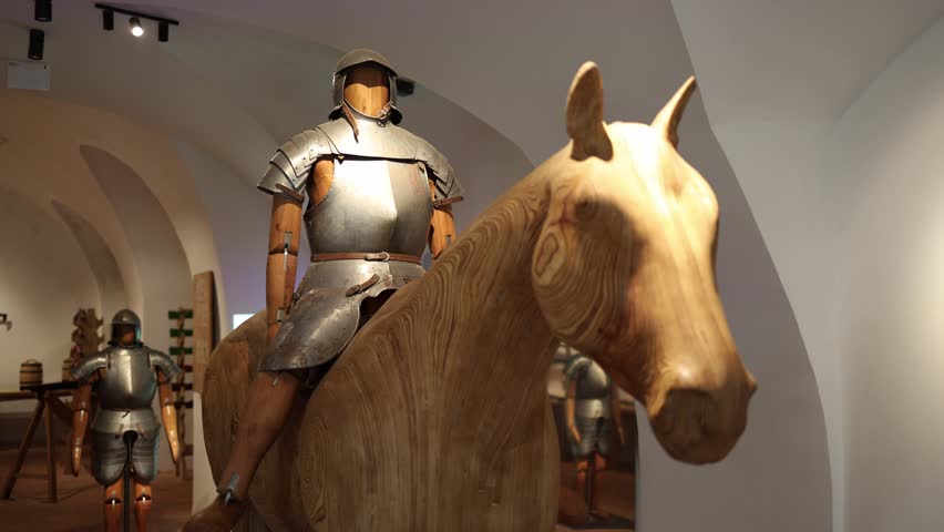 Wooden mannequin dressed in medieval armor riding a carved wooden horse displayed in a bright museum room creating an immersive scene of historical jousting and knightly culture