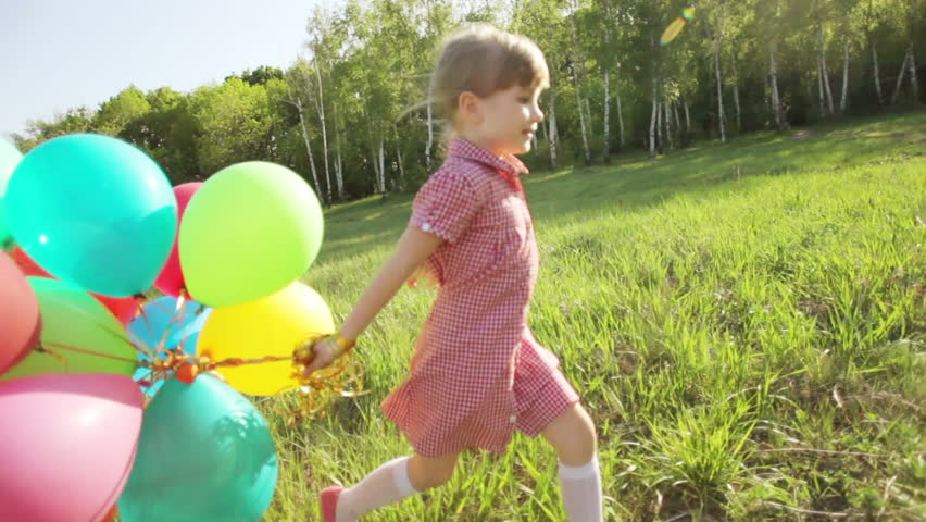 Child running with balloons in the park. Girl looking at camera
