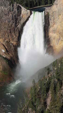Vertical orientation mobile format video of scenic waterfall. Lower Yellowstone Falls in the Grand Canyon of Yellowstone, Yellowstone National Park, Wyoming, USA. Featuring river, cliffs, forest, and 