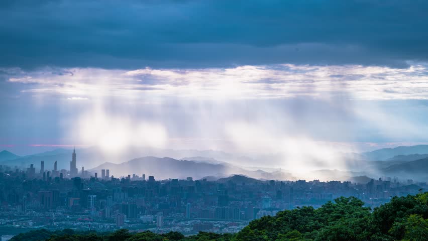 Stunning view from Dadao Mountain Shulin Taiwan. Dramatic light rays penetrate rain clouds over Taipei city skyline creating mystical atmosphere.