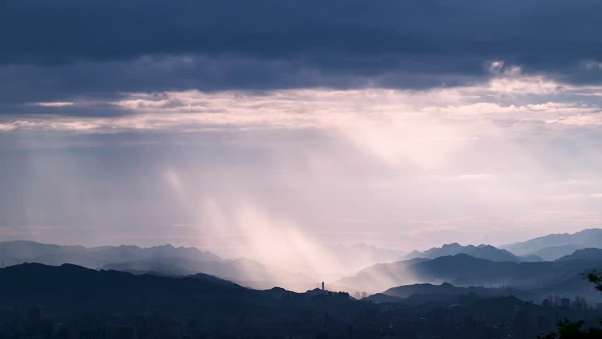 Stunning view from Dadao Mountain Shulin Taiwan. Dramatic light rays penetrate rain clouds over Taipei city skyline creating mystical atmosphere.