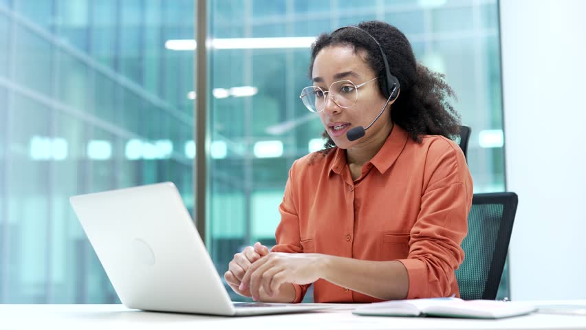 Confident african american businesswoman in wireless headset talking on video call conference using a laptop sitting in office. Female coach speaks remotely, communicates at online meeting, training