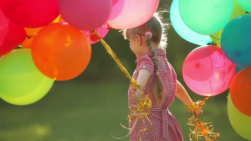 Child spinning with balloons in the park.  Girl looking at camera
