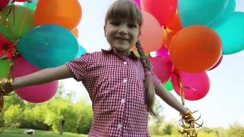 Child spinning with balloons in the park and looking at camera
