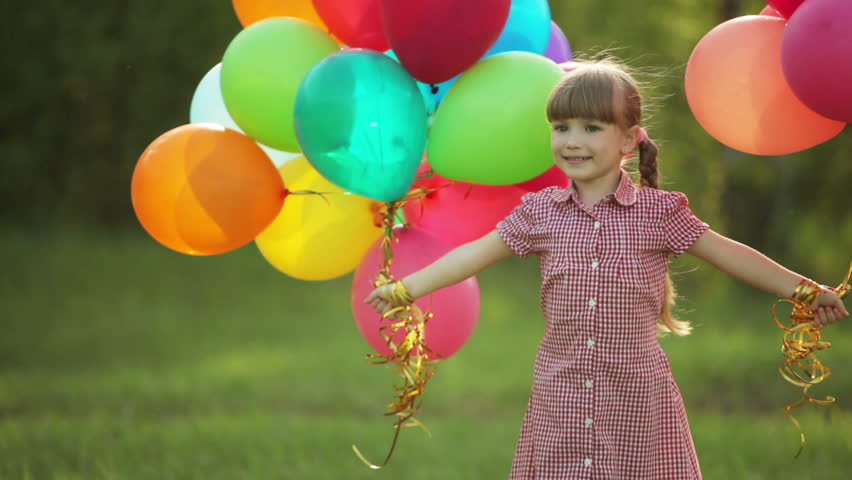 Girl spinning with balloons in the park and looking at camera
