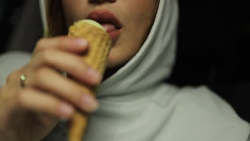 A woman eats an ice cream cone in a car in the evening