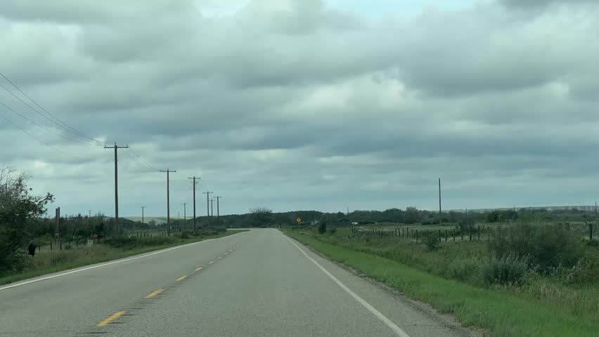 Driving along a rural highway in Alberta, Canada during summer, surrounded by open farmland, blue skies, and expansive prairie views.