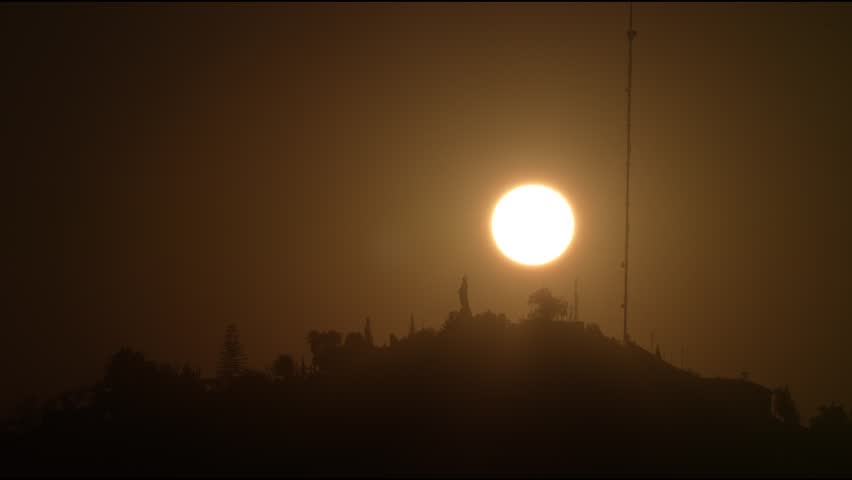 Sun setting behing a hill and a statue