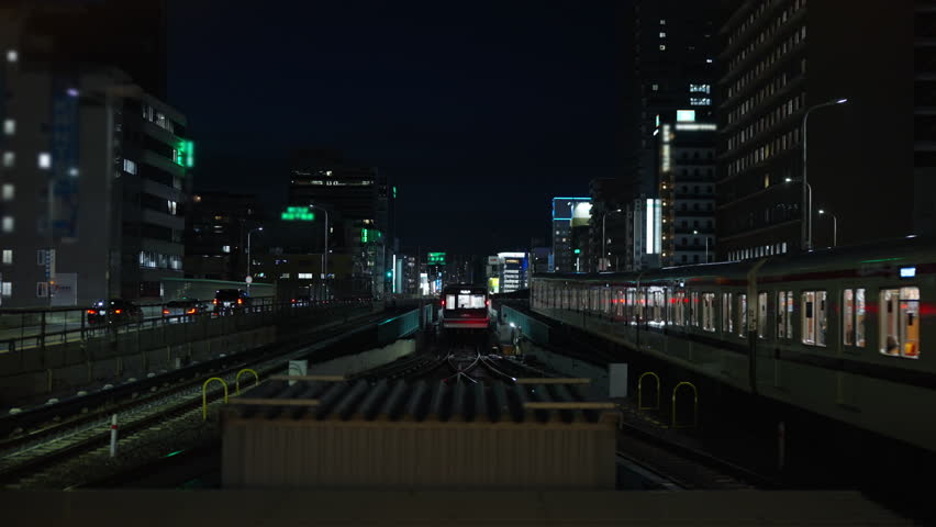 High angle view of Trains on railway tracks entering and leaving station platforms, flanked by busy highways and cityscape at night. Modern urban transportation and railway industry infrastructure.