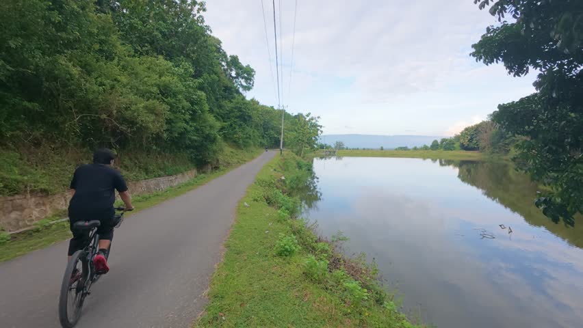Man Riding Bicycle on Road By Lake